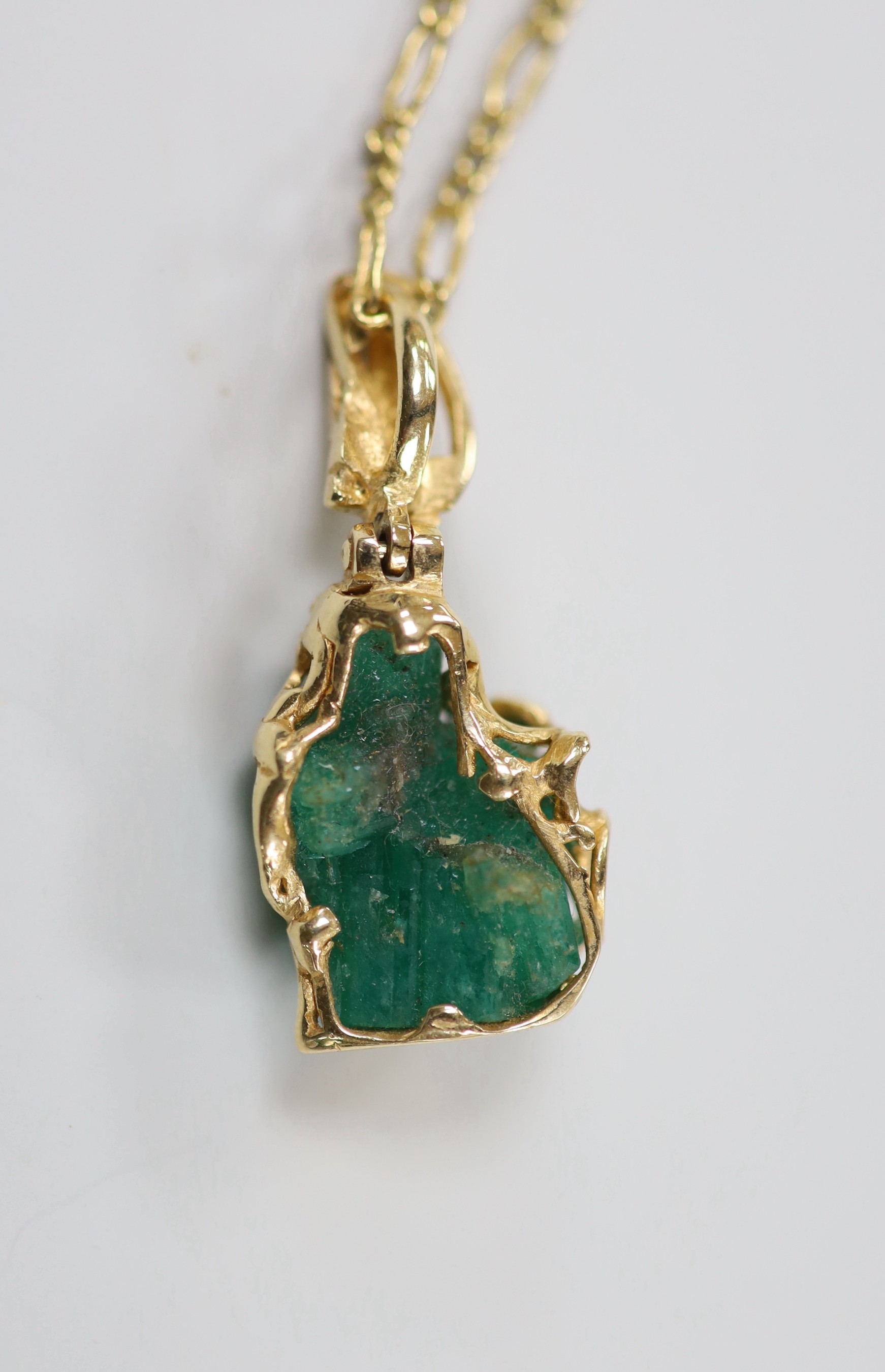 A yellow metal mounted carved emerald boulder set pendant, overall 34mm, gross weight 6 grams, on a gilt metal chain.